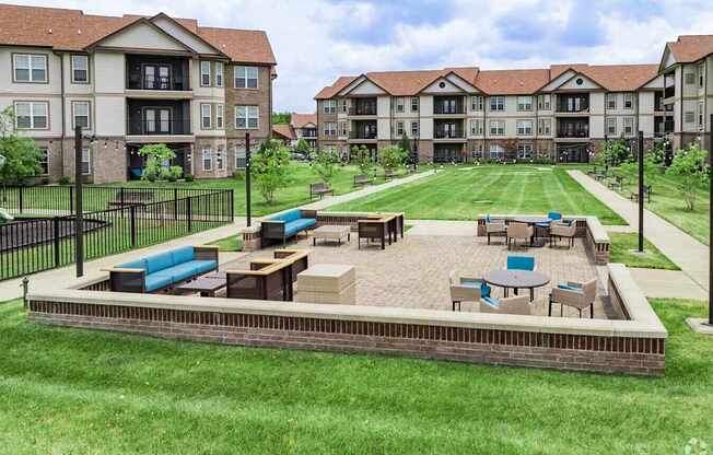 A large grassy area with a patio and chairs in front of apartment buildings.