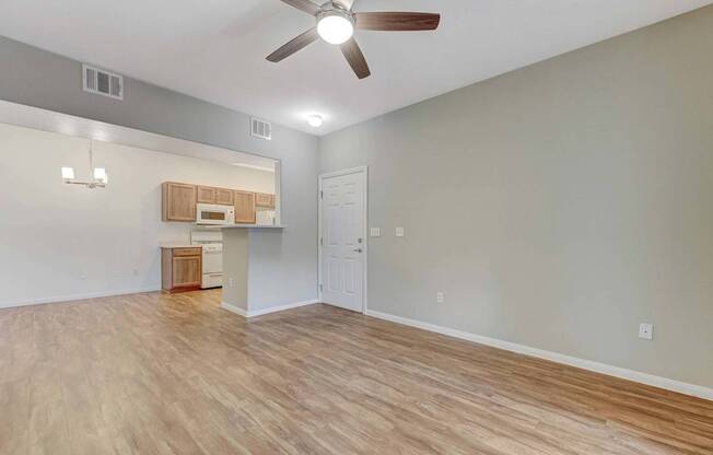A room with a ceiling fan and light fixture, a small kitchenette, and a door.