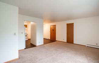 a living room with carpet and white walls and two doors. Fargo, ND Crown Court 1 Apartments