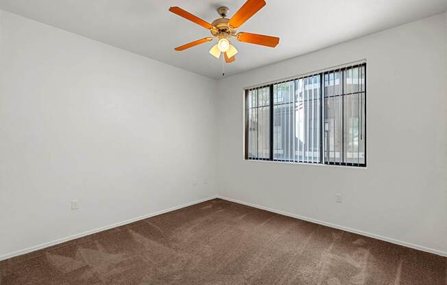 Empty room with a ceiling fan and a window with bars.