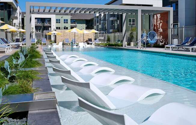 a pool with white chairs and a building in the background