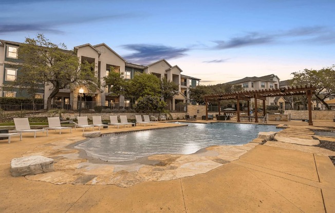 A large outdoor swimming pool surrounded by a stone patio and lounge chairs.