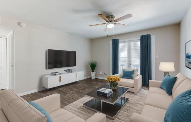 A living room with a white couch, a coffee table, and a flat screen TV mounted on the wall.