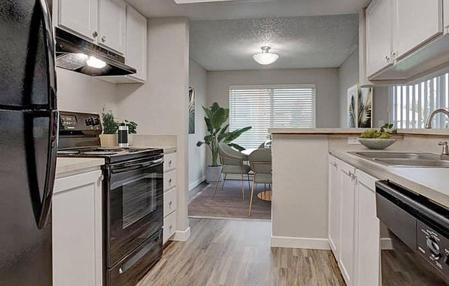 A kitchen with a full-size fridge, oven, stovetop, double bowl sink, and dishwasher. White top and bottom cabinets and a breakfast bar.