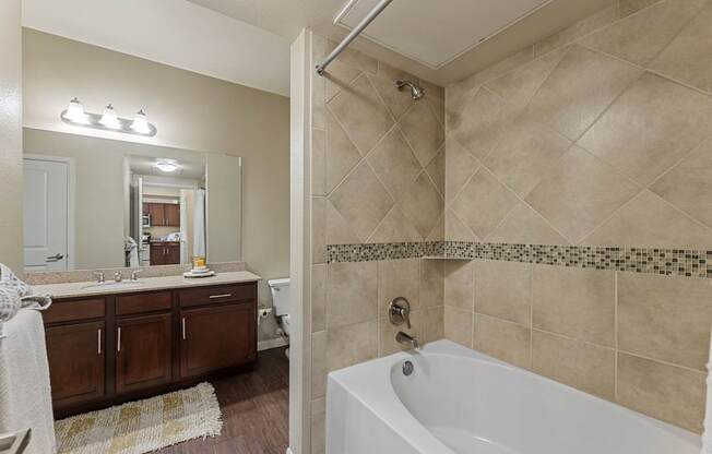 A bathroom with a white tub and brown cabinets.