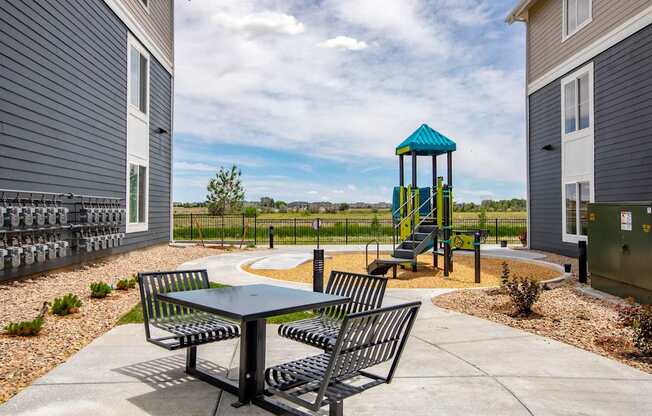 A playground with a blue and yellow tower and a table and chairs in the foreground.