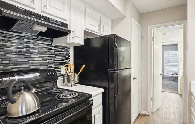 Model A2 floor plan kitchen with black appliances, tile backsplash, and white cabinets Noel on The Parkway in Dallas, TX