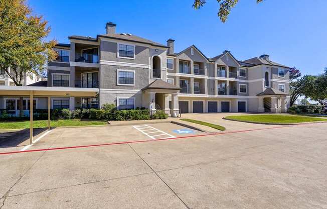 A three-story apartment building with attached garages and carport parking spaces at Saxony at Chase Oaks Apartments in Dallas, TX, offering modern conveniences in a beautifully maintained setting.