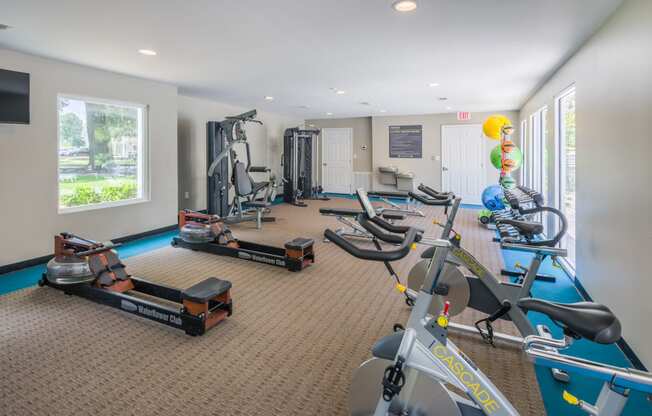 a gym with a lot of exercise equipment and a window with a view of the water