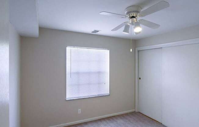 Bedroom with white walls, grey carpet, white closets, a large window, and a ceiling fan.