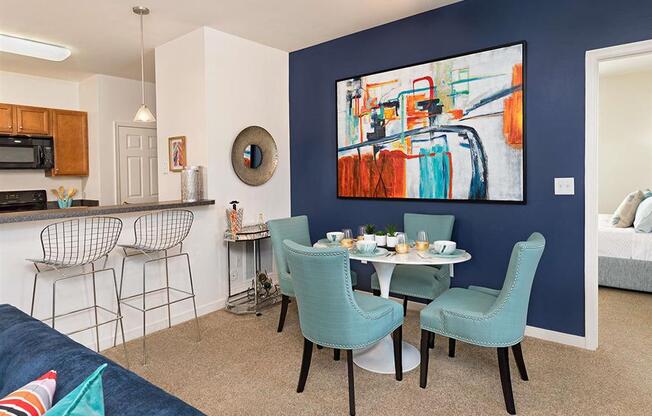 a dining area with a table and chairs and a kitchen in the background