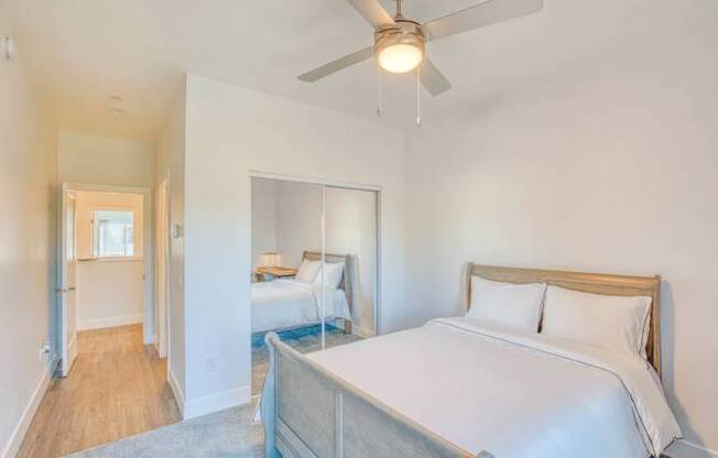 A bedroom with a bed, a ceiling fan, and a mirror.