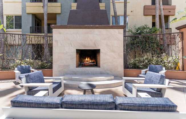 A fireplace is in the middle of a patio with blue cushioned chairs around it at The Kitt at Warner Center Apartments, California, 91303