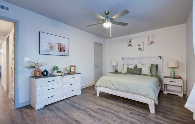 A bedroom with a bed, nightstand, and a white dresser.
