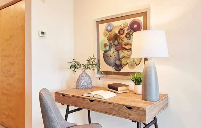 A grey chair in front of a wooden desk with a lamp and a painting on the wall.