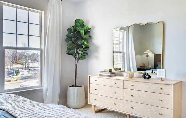 A bedroom with a large window, a white dresser, and a mirror.