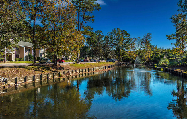 A serene pond with a fountain in the middle surrounded by trees and buildings.