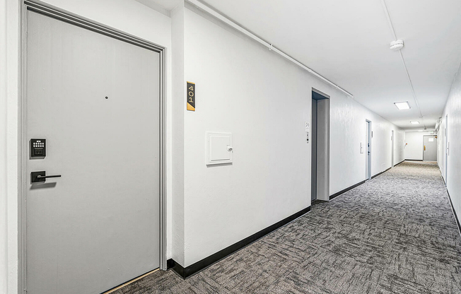 Sleek modern apartment hallway featuring stylish gray doors, secure keypad entry, and sophisticated carpeted flooring.