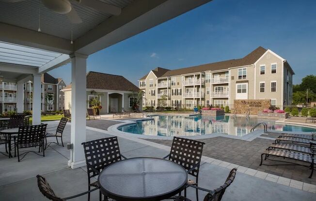 A pool area with chairs and a table in front of apartment buildings.at Meridian West Shore, Pennsylvania 17055