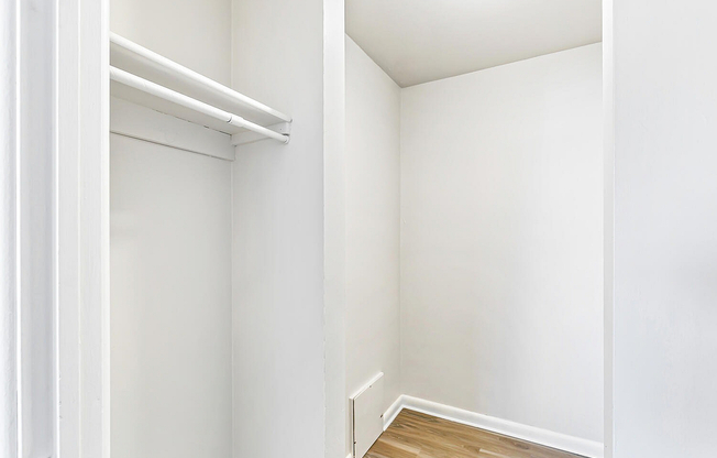Bright and spacious walk-in closet with sleek white walls and hardwood flooring, perfect for ample storage.