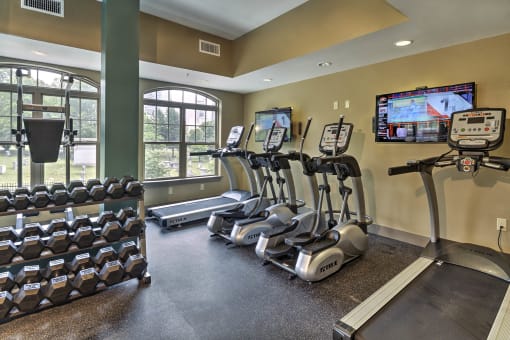 a gym with cardio machines and a tv