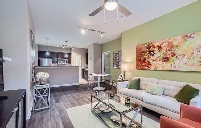 A living room with a glass coffee table and a painting on the wall.