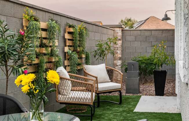 a backyard patio with two chairs and a table and a vase of flowers