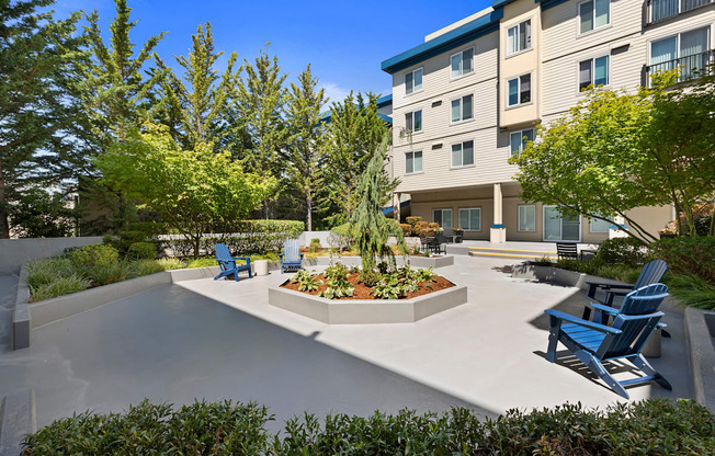 a courtyard with a large tree in the center and a seating areas with blue Adirondack chairs at Guinevere Apartment Homes, Seattle