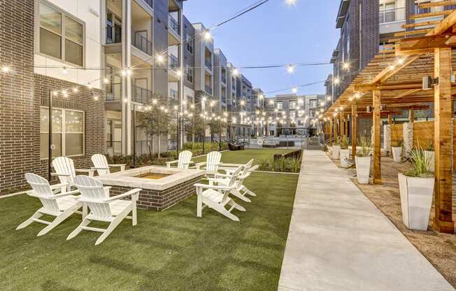 Luxury Apartments For Rent In Austin - Arise Riverside - Courtyard With Lush Lawn And Potted Plants, Lounging Area, Firepit, String Lights, And Chairs.