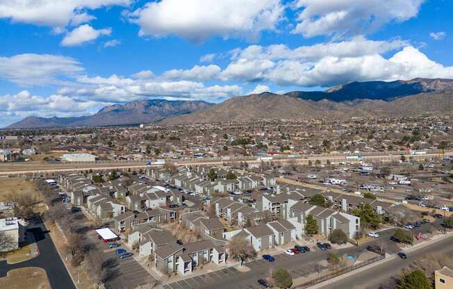 A residential area with houses and cars under a blue sky with clouds.