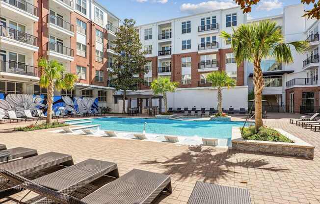 A pool surrounded by lounge chairs and palm trees at The Grand At Upper Kirby in Houston, TX