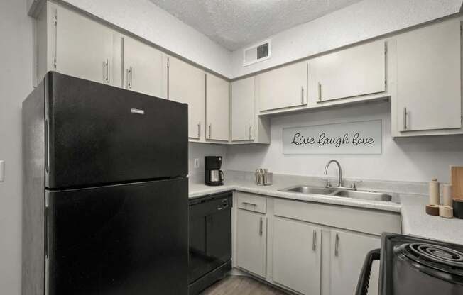A black refrigerator in a kitchen with a sign that says Live Laugh Love.