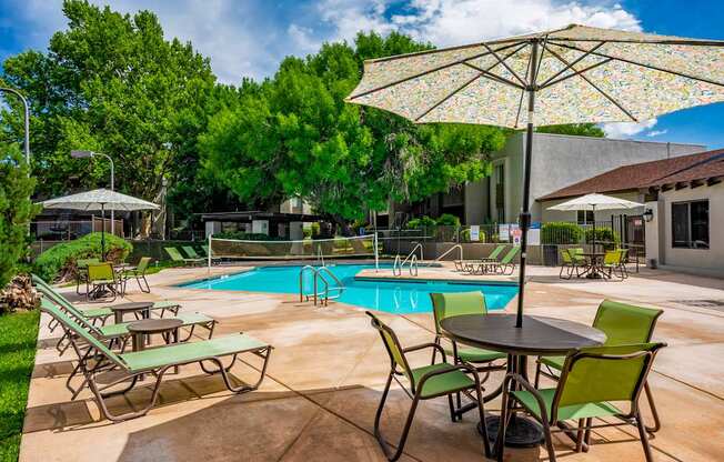 A poolside area with a table, chairs, and an umbrella.