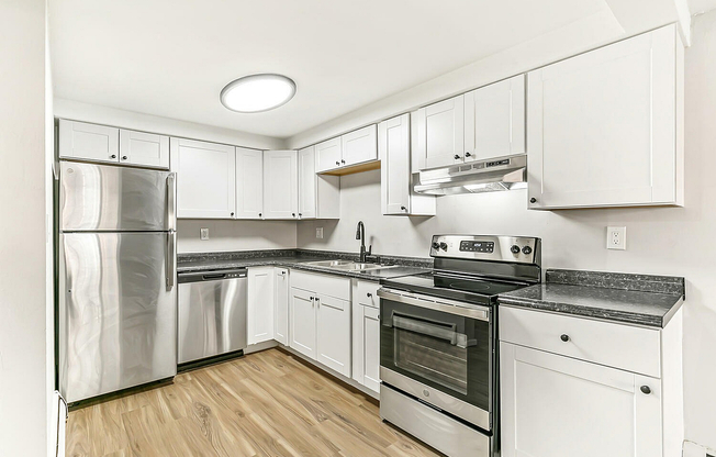 Modern kitchen with sleek stainless steel appliances, elegant white cabinetry, and beautiful wood flooring.