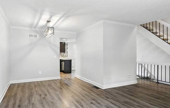 A spacious room with wooden floors and a staircase with a black railing.