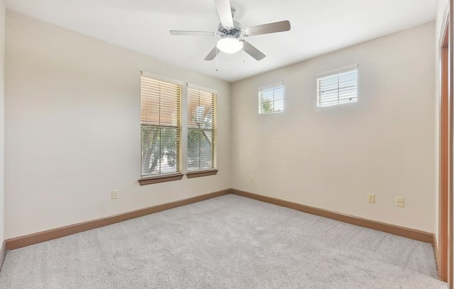 an empty room with a ceiling fan and two windows