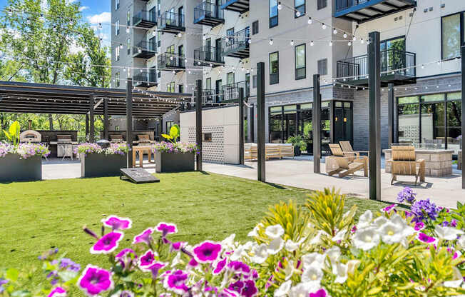 A patio area with a table and chairs is surrounded by a grassy area with purple flowers.