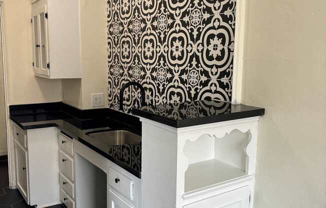 a kitchen with black counter tops and white cabinets and a black and white wallpaper