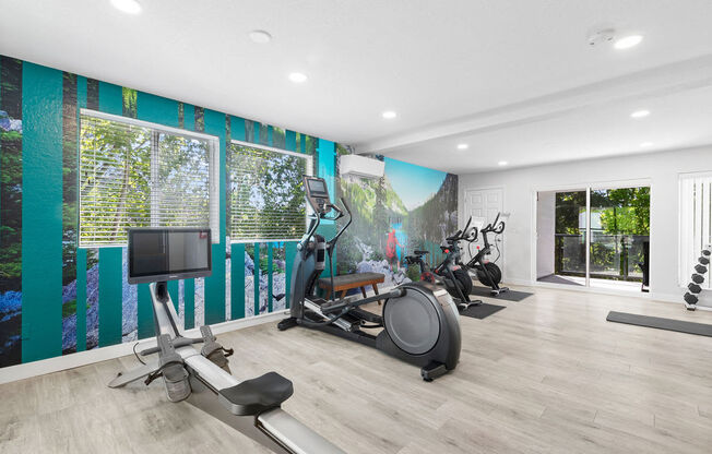 the gym has plenty of exercise equipment and a mural on the wall