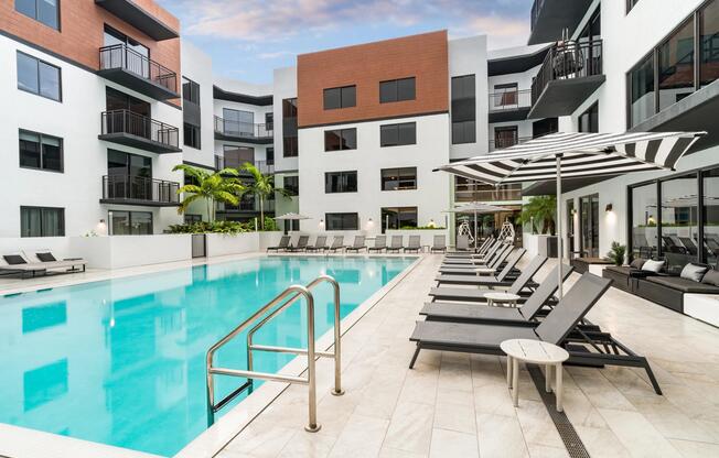 Resort-style pool courtyard with sun loungers, shaded seating, and palm-lined surroundings designed for outdoor relaxation and social connection.
