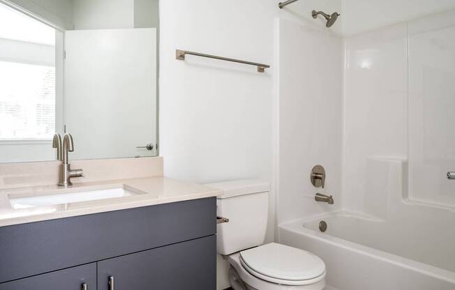 A white toilet sits in a bathroom with a white tub and sink.