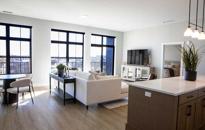 A modern living room with a white couch, a wooden cabinet, and a large window overlooking the city.