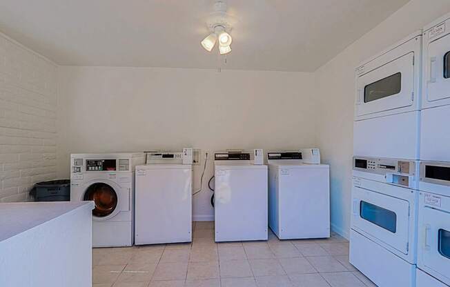 A laundry room with a white brick wall and a row of washing machines.