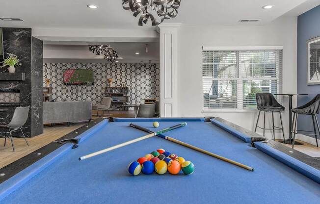 A pool table with a blue cloth and several pool balls and cues.