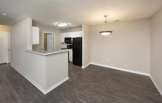 an empty living room with a kitchen and a dark wood floor