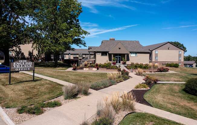 The Olde English Village clubhouse exterior is surrounded by well-maintained landscaping, creating a welcoming central gathering space for residents.