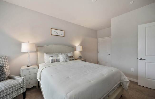 A bedroom with a large bed, a chair, and two lamps.