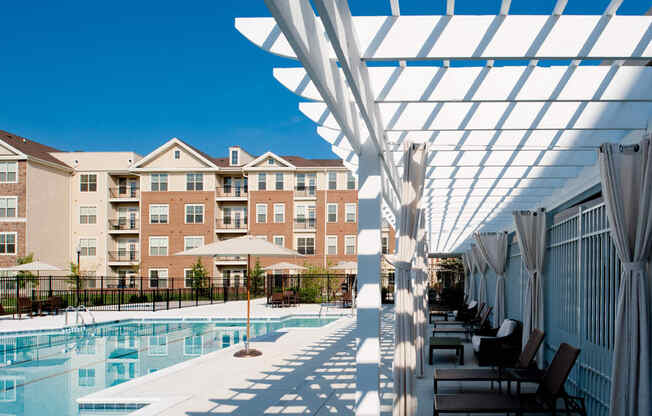 a swimming pool with chairs under a white canopy in front of an apartment building