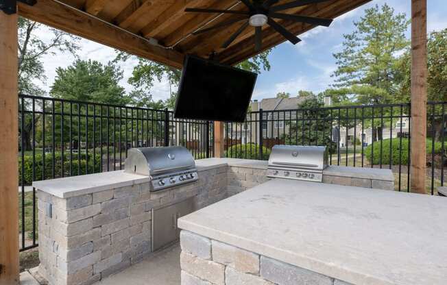 a stone outdoor entertaining area with a stone grill and a tv