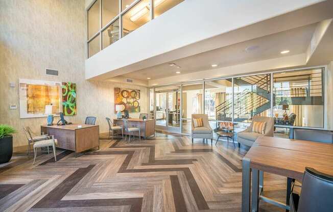 A modern leasing office lobby here at Lakewood on the Trail with wood plank flooring, work desks, cozy seating chairs, glass walls, and a bright open layout with a welcoming, professional feel.